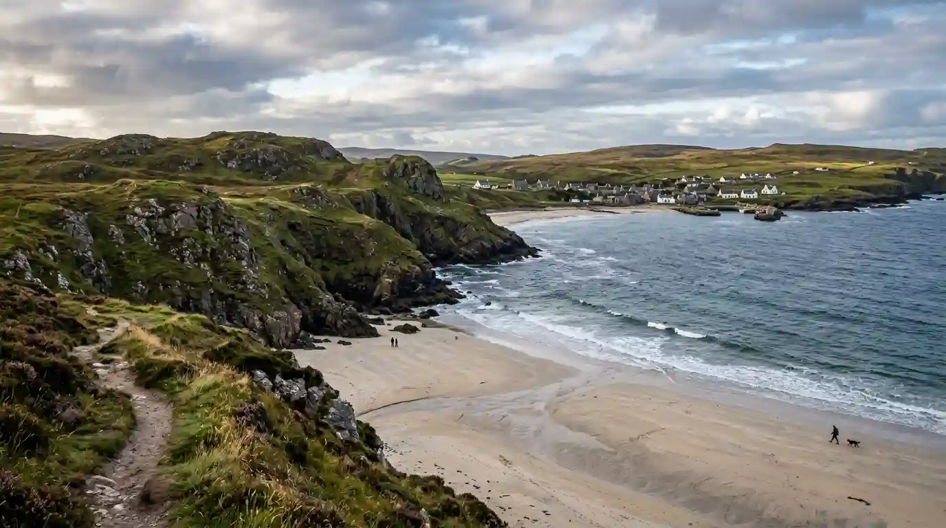 Sandy Scottish coastline with rugged green headlands and a traditional coastal village beside the sea.